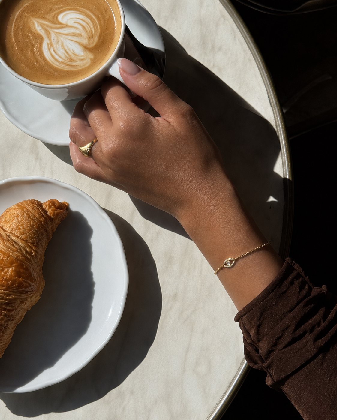 Tiye armbånd i forgyldt sterlingsølv med evil eye-vedhæng, fotograferet på café