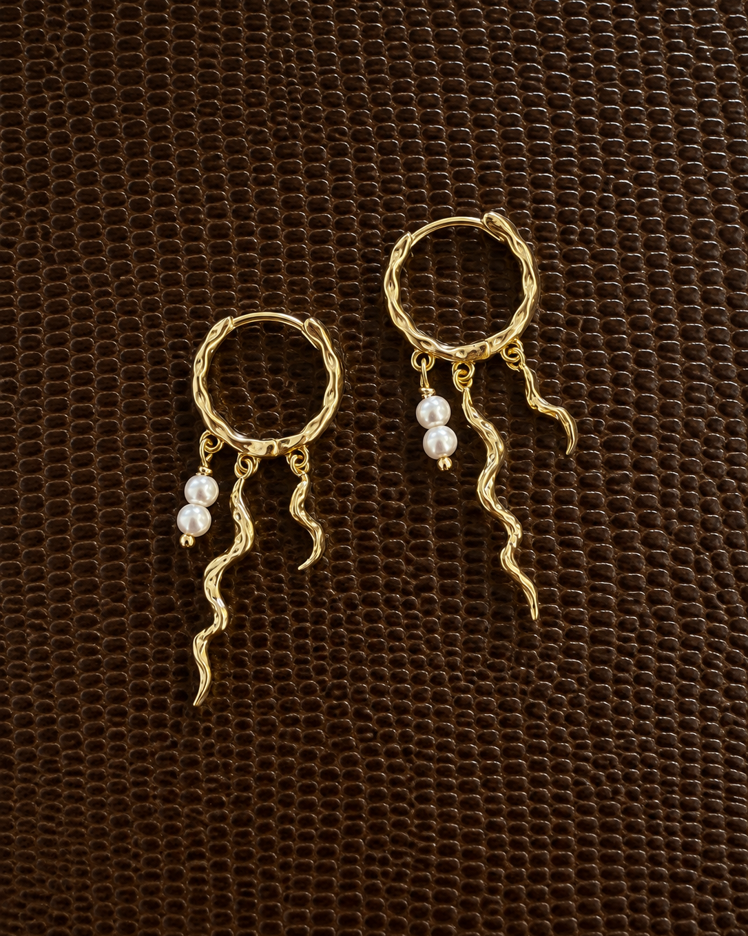 Close-up of Delmar earrings with an asymmetric, wavy design in a gold-plated version
